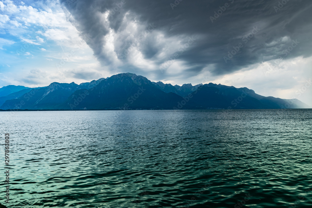 Landscape of Alps mountains,lake Geneva,cloudy dark sky with rain in the distance. Shot taken from the shore of the lake in Montreux, Switzerland. 