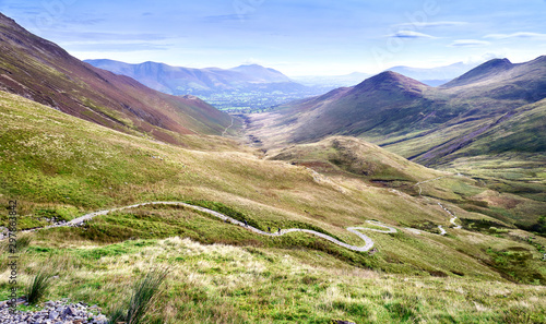Three distant hikers walking up a winding rocky path from Coledale Beck that leads to Hopegill Head, Crag Hill and Grasmoor in the Lake District.