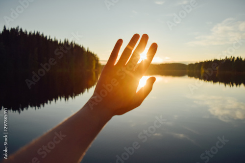 Blurred human hand reaching for the sun everning sun, at the lake in Finland photo