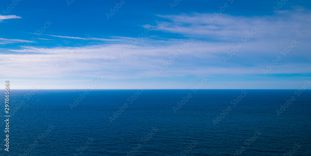 Obraz premium the blue ocean meeting the blue sky with clouds on the horizon 