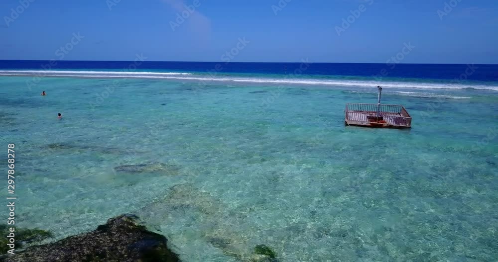 Aerial view above clear tropical water with underwater algae and reefs, looking out towards a few tourists and an old floating dock in the Maldives Aerial view above clear tropical water with underwater algae and reefs, looking out towards a few tourists and an old floating dock in the Maldives