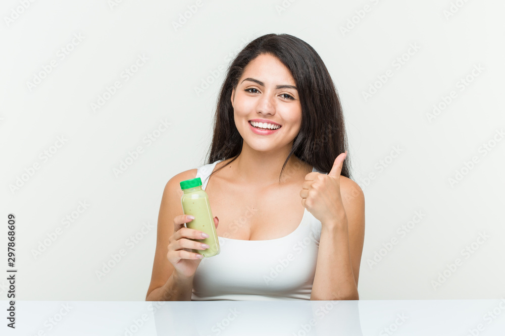 Young hispanic woman holding a vegetable drink smiling and raising thumb up Young hispanic woman holding a vegetable drink smiling and raising thumb up