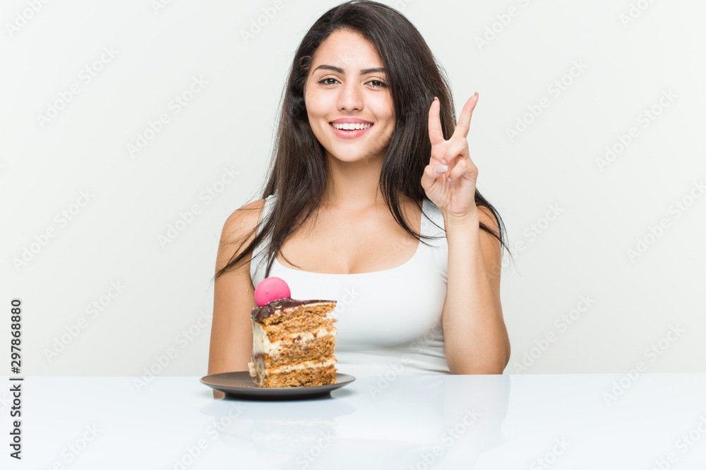 Young hispanic woman eating a cake showing number two with fingers. Young hispanic woman eating a cake showing number two with fingers.