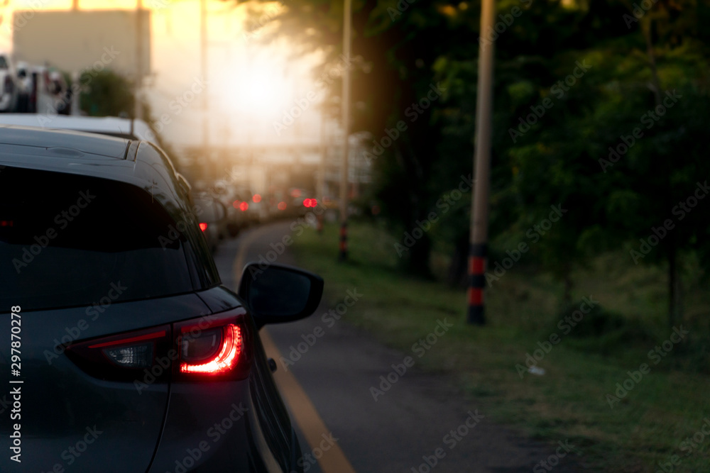 Obraz premium In the evening traffic conditions with long queues of cars and turning on brake lights.With trees, grass, and electric poles illuminating the side.