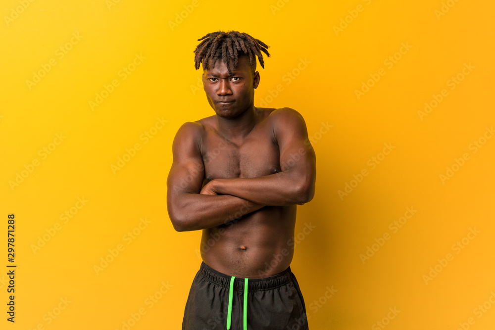 Fototapeta premium Young black man shirtless wearing swimsuit unhappy looking in camera with sarcastic expression.