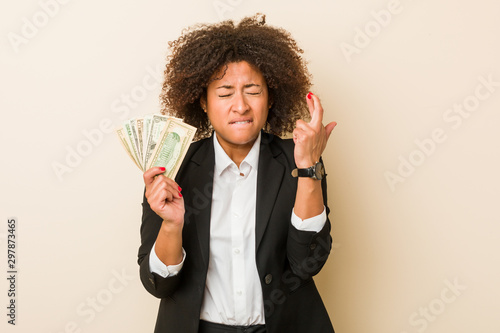 Young african american woman holding dollars crossing fingers for having luck photo