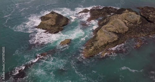 Drone aerial view of the coastline of Cornwall looking down at a large formation of rocks with waves crashing against them photo