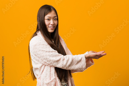 Young chinese woman in pajama holding a copy space on a palm. © Asier