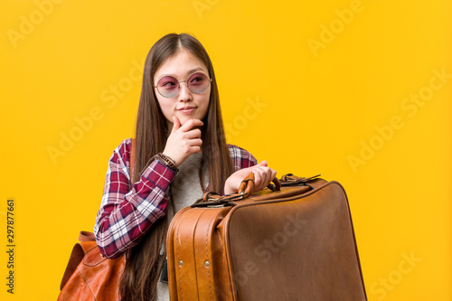 Young asian woman holding a suitcase looking sideways with doubtful and skeptical expression. photo