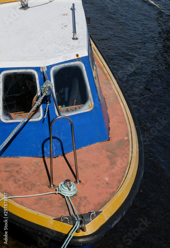 View of an old boat moored at a dock from above in white, blue & orange with dark water. © Michaella