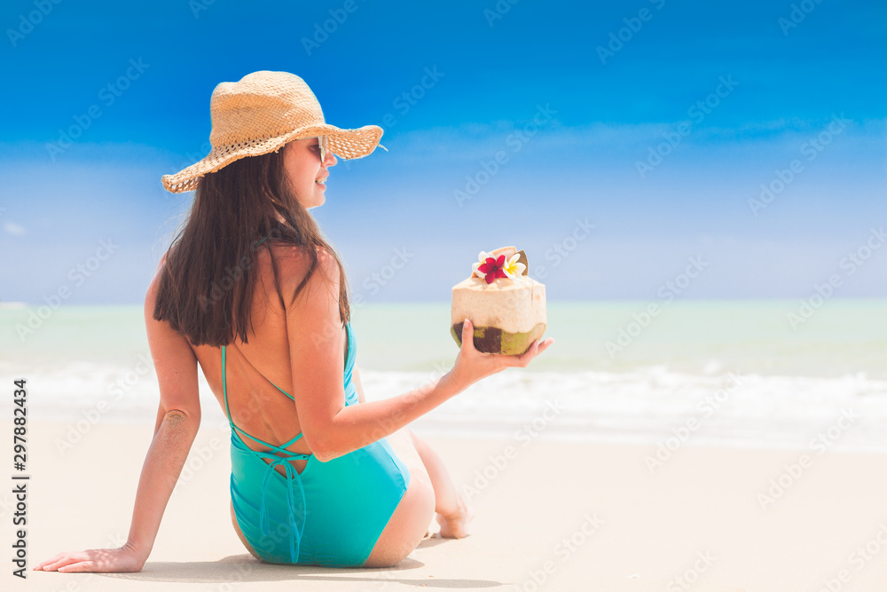woman in bikini lying on tropical beach with coconut cocktail
