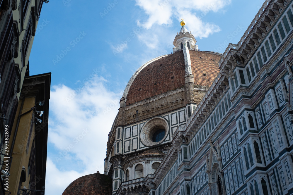 Florence's Santa Maria del Fiore Dome seen from the side with clouds and blue sky.