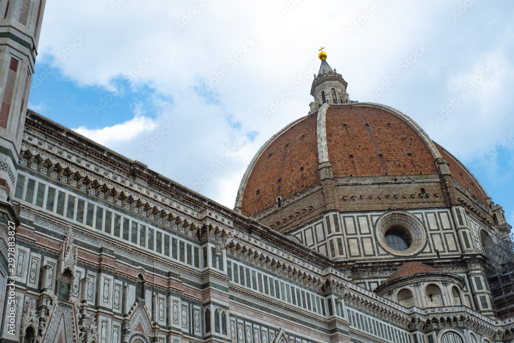 Florence's Santa Maria del Fiore Dome seen from the side with clouds and blue sky.