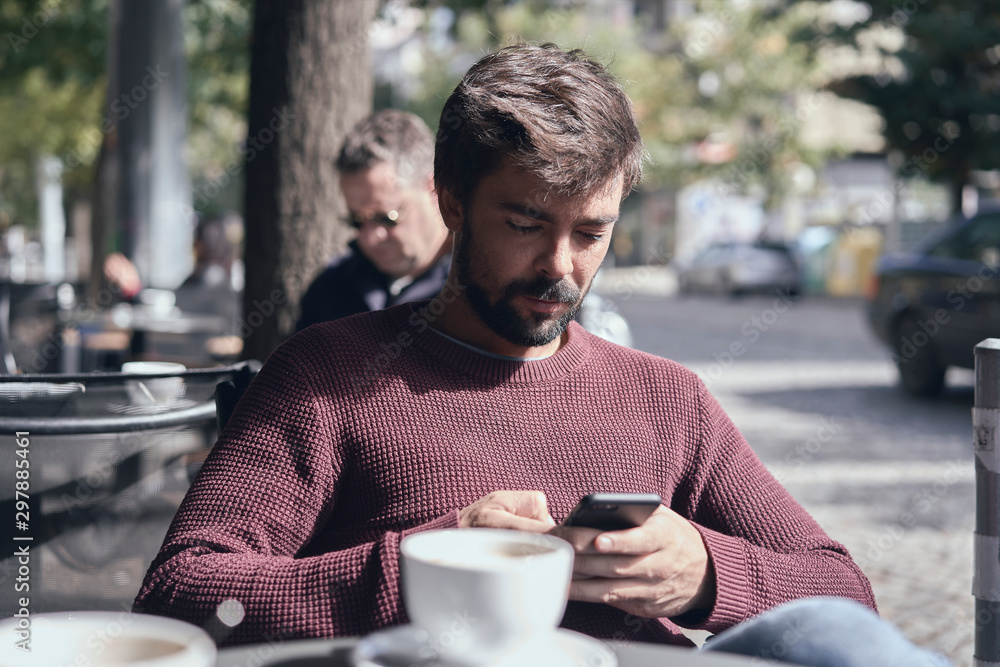 Attractive young bearded man using his smartphone in the cafe Attractive young bearded man using his smartphone in the cafe