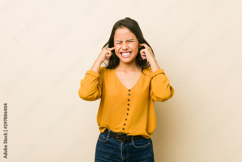 Young hispanic woman against a beige background covering ears with hands. Young hispanic woman against a beige background covering ears with hands.