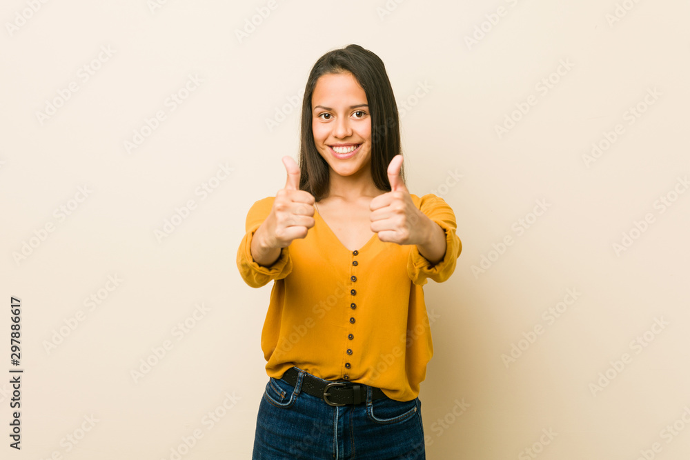 Young hispanic woman against a beige background with thumbs ups, cheers about something, support and respect concept. Young hispanic woman against a beige background with thumbs ups, cheers about something, support and respect concept.