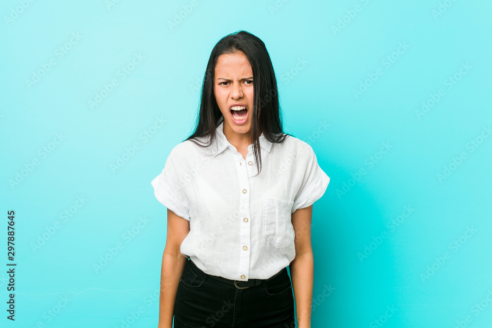 Fototapeta premium Young hispanic cool woman against a blue wall screaming very angry and aggressive.