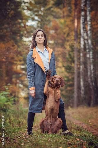 Happy young woman with a hungarian viszla in the autumn forest