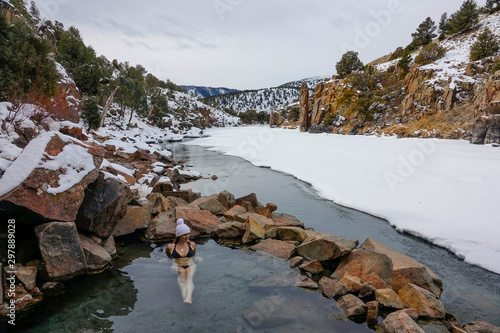 Fotografie Young woman in bikini lies in Radium hot springs and observes snowy landscape