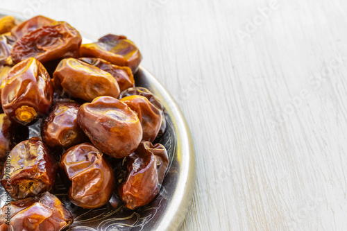 Dates lie on a silver tray on a white wooden background, side view from above