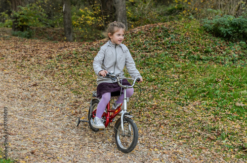 Fototapeta Naklejka Na Ścianę i Meble -  Little happy girl child rides a bicycle in the autumn forest