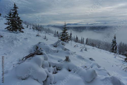 Magic winter fogs in Ukrainian Carpathians overlooking the snow-capped mountain peaks from the picturesque mountain valley with tourists in tents.