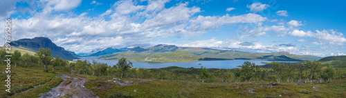 Panoramic landscape with beautiful river Lulealven, snow capped mountain, birch tree and footpath of Kungsleden hiking trail near Saltoluokta, north of Sweden, Lapland wild nature. Summer blue sky
