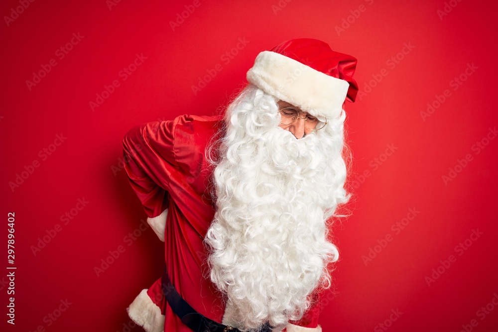 Middle age handsome man wearing Santa costume standing over isolated red background Suffering of backache, touching back with hand, muscular pain