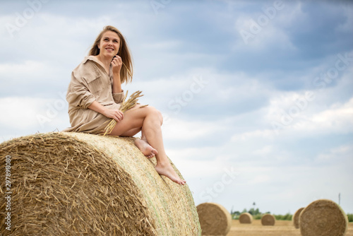 Beautiful happy woman seating on a haystack.
