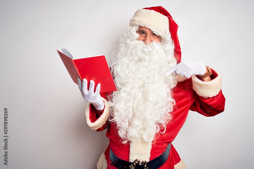 Middle age man wearing Santa Claus costume reading book over isolated white background looking confident with smile on face, pointing oneself with fingers proud and happy.