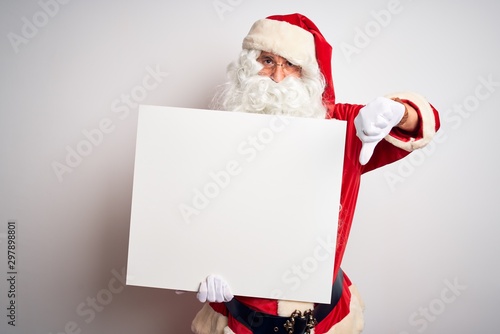 Middle age man wearing Santa Claus costume holding banner over isolated white background with angry face, negative sign showing dislike with thumbs down, rejection concept © Krakenimages.com