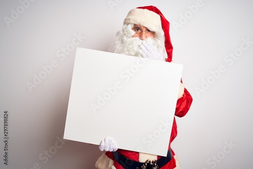 Middle age man wearing Santa Claus costume holding banner over isolated white background cover mouth with hand shocked with shame for mistake, expression of fear, scared in silence, secret concept © Krakenimages.com