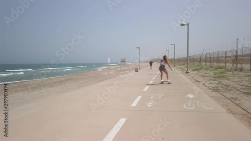 Young athletic woman surf-skating down the Tel aviv beach promenade on a bright sunny morning. Following shot with the mediterranean sea in the background. 