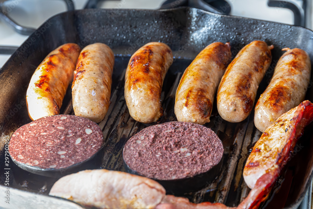 Sausages, bacon and black pudding cooking in a griddle pan Stock Photo