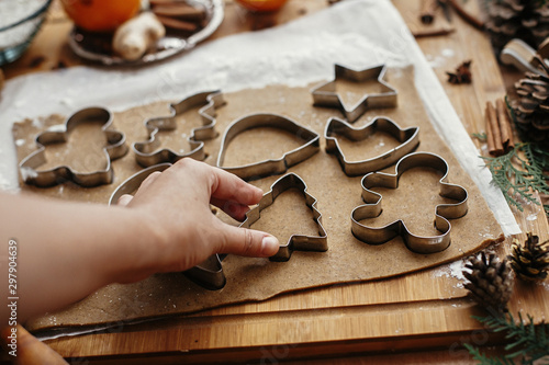 Making christmas gingerbread cookies. Hand cutting raw dough with  metal cutters and anise, ginger, cinnamon, pine cones, fir branches on rustic table.