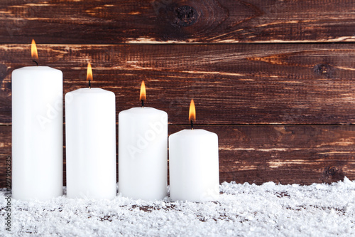 Christmas candles with white snow on brown wooden background