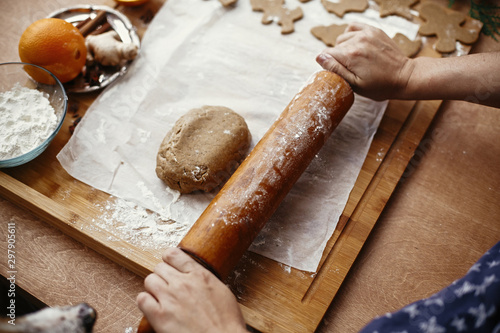 Hands rolling raw dough with wooden rolling pin on background of metal cutters, anise, ginger, cinnamon, pine cones, fir branches on rustic table.Making christmas gingerbread cookies. photo