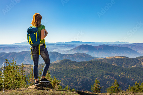 Rear view of female hiker with backpack standing on top of the mountain and enjoying the view during the day. photo