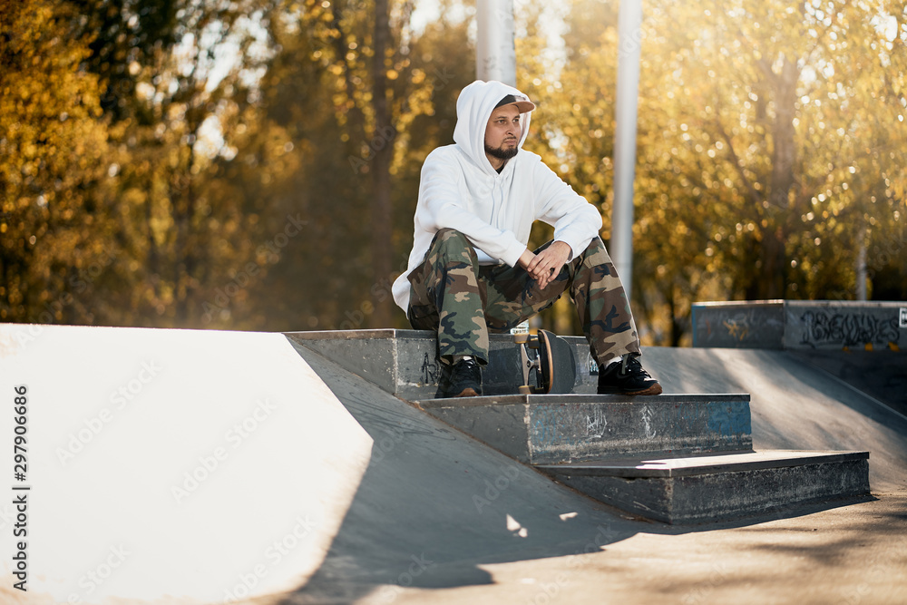 Man in skatepark with skateboard on warm autumn day
