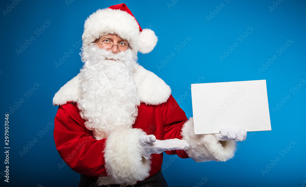 Look! Real Santa is pointing with his right hand at the blank postcard with copyspace on it, which he holds in his left hand, looking at the camera calmly. Look! Real Santa is pointing with his right hand at the blank postcard with copyspace on it, which he holds in his left hand, looking at the camera calmly.