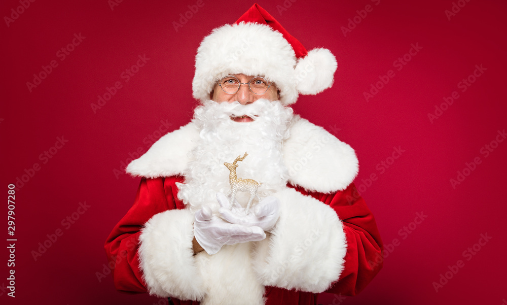 Christmas miracle. Santa Claus is posing with a golden deer figurine in his hands, smiling and looking towards the camera. Christmas miracle. Santa Claus is posing with a golden deer figurine in his hands, smiling and looking towards the camera.