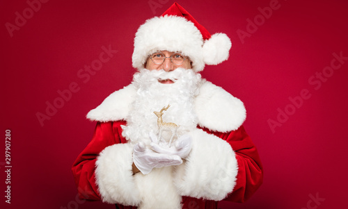 Christmas miracle. Santa Claus is posing with a golden deer figurine in his hands, smiling and looking towards the camera.