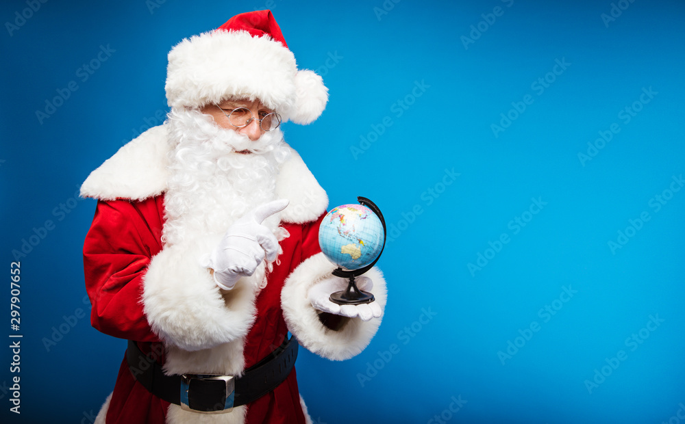 A new destination to visit. Close up photo of Santa Claus choosing with his right index finger a destination where to go on the globe, which is standing on his left hand. A new destination to visit. Close up photo of Santa Claus choosing with his right index finger a destination where to go on the globe, which is standing on his left hand.
