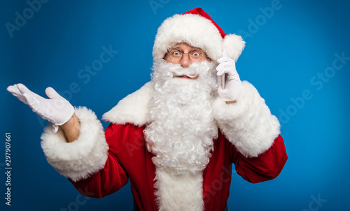 This can   t be  Authentic Santa Claus is posing while talking on the cellphone  which he holds in his left hand  spreading his right hand in surprise.