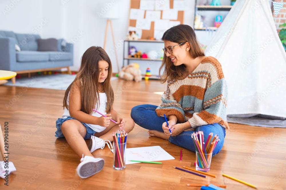Beautiful teacher and toddler drawing using pencils and paper around lots of toys at kindergarten Beautiful teacher and toddler drawing using pencils and paper around lots of toys at kindergarten