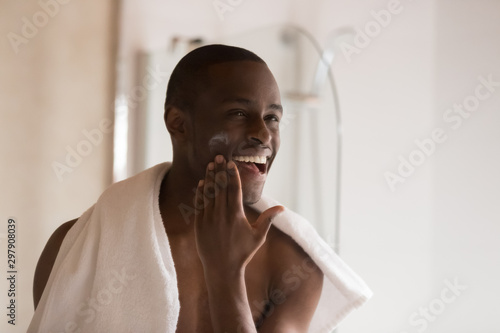 Fotografie Happy smiling african ethnicity man applying moisturizing balm on cheek