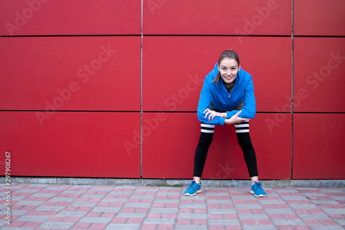 sporty girl is training against a red wall in the street, a woman is doing warm-up in sportswear outdoors, copy space