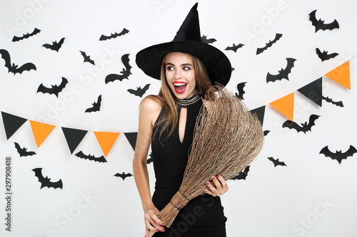 Beautiful woman in halloween costume holding broom with paper bats and flags on white background