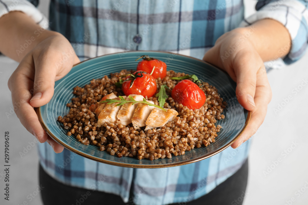 Woman holding plate of buckwheat porridge with meat and tomatoes, closeup Woman holding plate of buckwheat porridge with meat and tomatoes, closeup