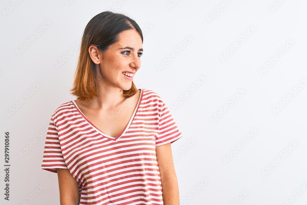Beautiful redhead woman wearing casual striped red t-shirt over isolated background looking away to side with smile on face, natural expression. Laughing confident. Beautiful redhead woman wearing casual striped red t-shirt over isolated background looking away to side with smile on face, natural expression. Laughing confident.